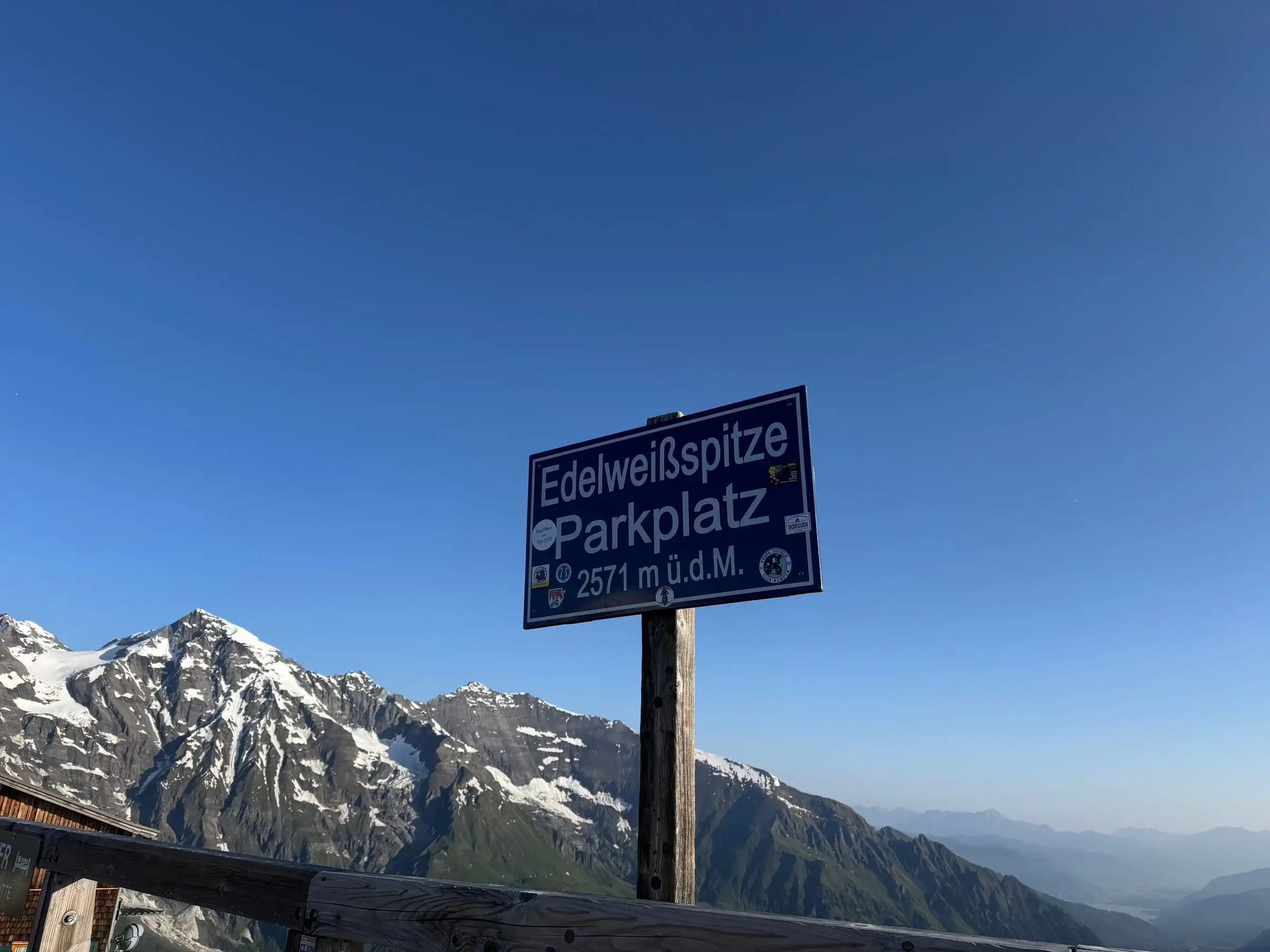 Cedule parkoviště Edelweißspitze (2571 m) na Grossglockneru, za ní zasněžené štíty.