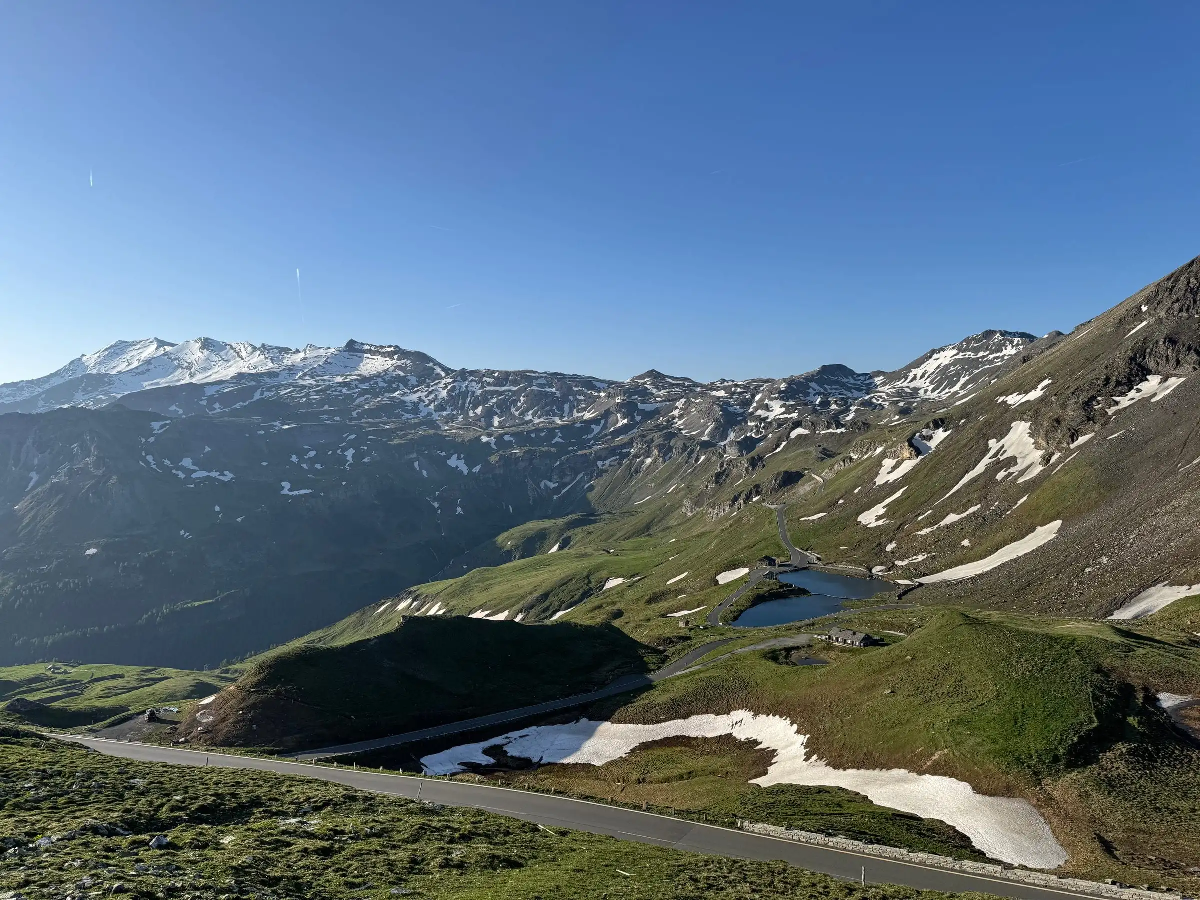 Vysokohorská silnice Grossglockner pod horami s ostrůvky sněhu a malým jezerem.